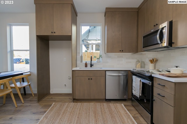 kitchen with light brown cabinets, light hardwood / wood-style floors, tasteful backsplash, appliances with stainless steel finishes, and sink