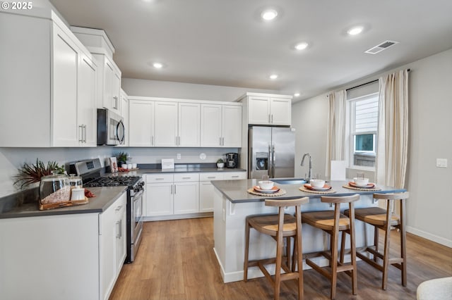 kitchen featuring light hardwood / wood-style floors, an island with sink, appliances with stainless steel finishes, white cabinets, and sink