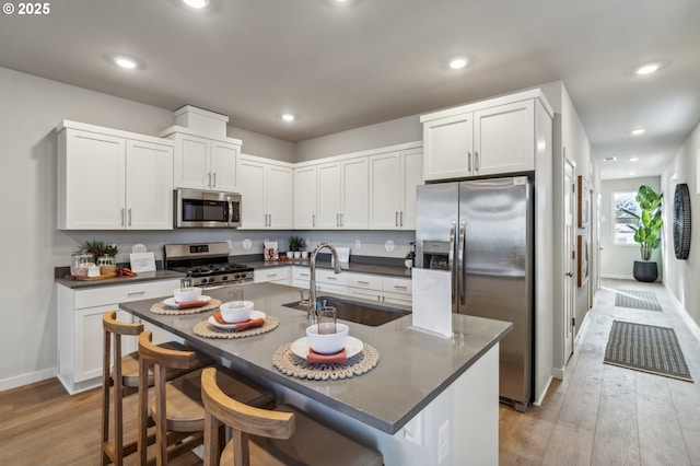 kitchen with stainless steel appliances, sink, a kitchen island with sink, light wood-type flooring, and a breakfast bar