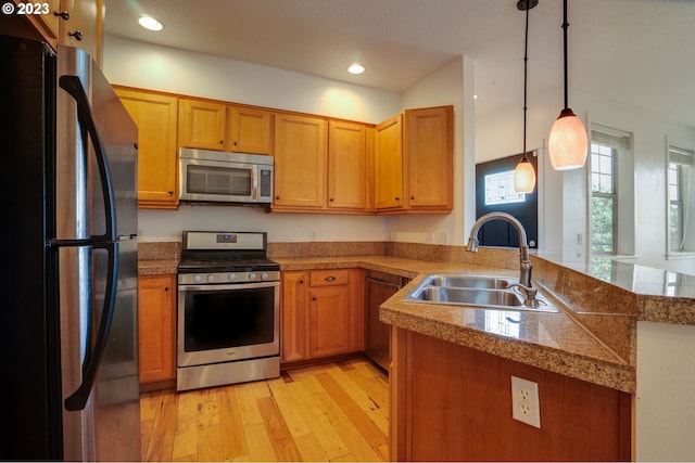 kitchen with kitchen peninsula, decorative light fixtures, appliances with stainless steel finishes, sink, and light hardwood / wood-style flooring