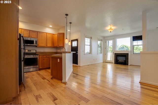 kitchen featuring pendant lighting, sink, a premium fireplace, appliances with stainless steel finishes, and light hardwood / wood-style flooring