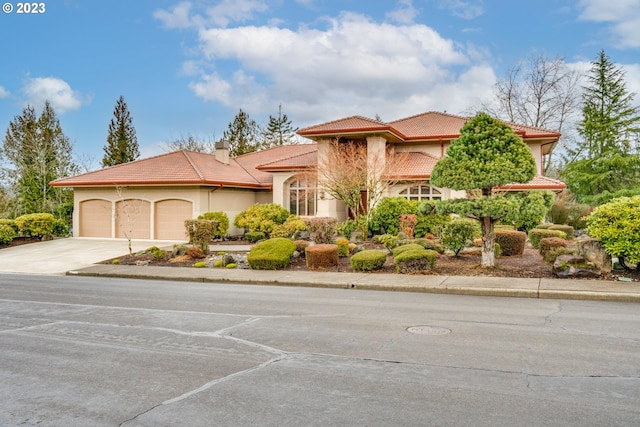 mediterranean / spanish-style house featuring concrete driveway, a tiled roof, an attached garage, and stucco siding