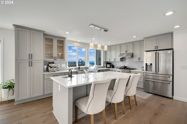 kitchen with under cabinet range hood, gray cabinetry, stainless steel appliances, and an island with sink