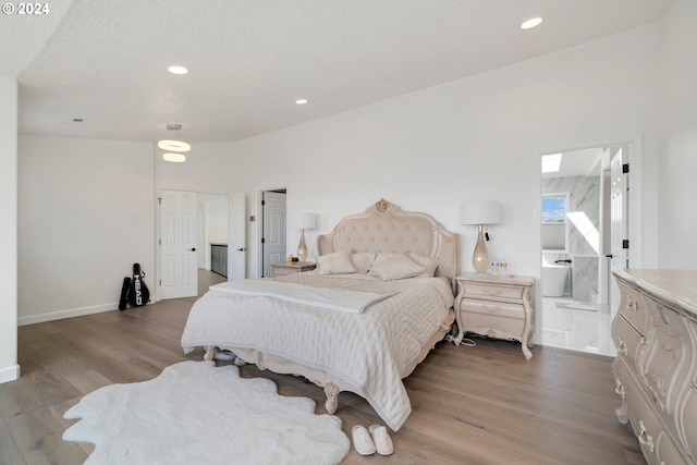 bedroom featuring baseboards, recessed lighting, wood finished floors, ensuite bath, and a textured ceiling