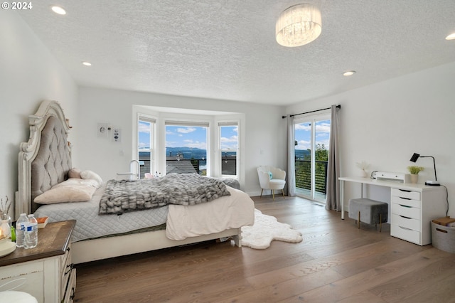 bedroom featuring access to exterior, recessed lighting, wood finished floors, and a textured ceiling