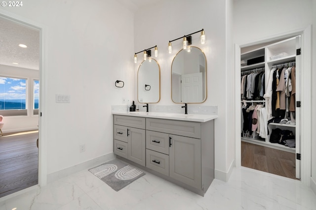 bathroom with baseboards, double vanity, a spacious closet, a textured ceiling, and marble finish floor