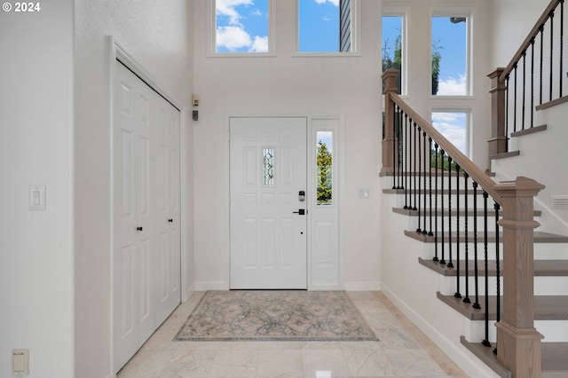 entrance foyer with baseboards, plenty of natural light, marble finish floor, and a towering ceiling