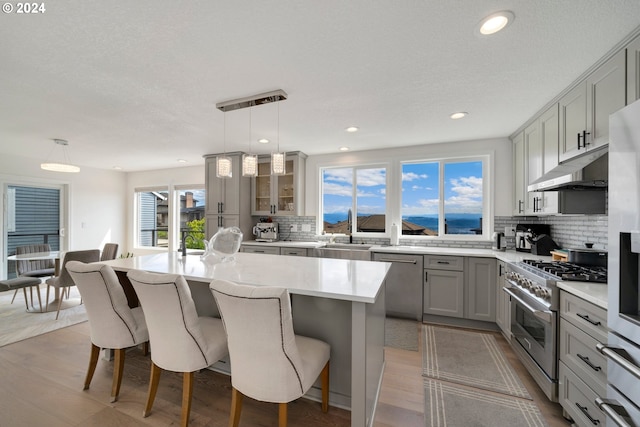 kitchen featuring under cabinet range hood, appliances with stainless steel finishes, a breakfast bar, and gray cabinetry