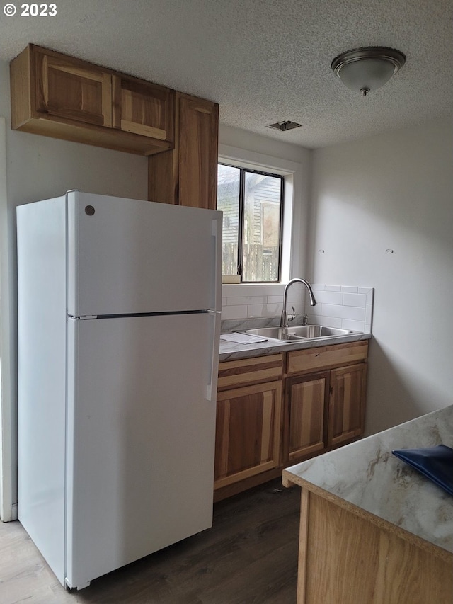 kitchen with a textured ceiling, white fridge, sink, and light wood-type flooring