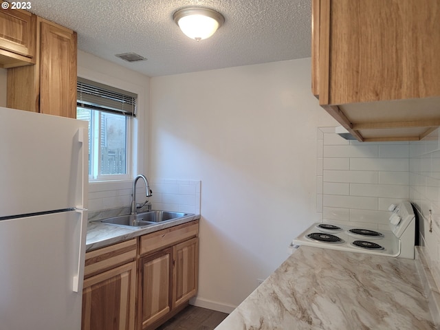 kitchen featuring backsplash, white fridge, sink, a textured ceiling, and stove