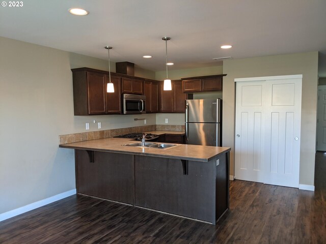 kitchen featuring kitchen peninsula, hanging light fixtures, dark hardwood / wood-style flooring, a breakfast bar, and stainless steel appliances