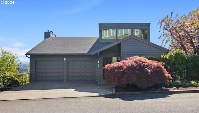 view of front facade with fence, driveway, a shingled roof, a chimney, and a garage