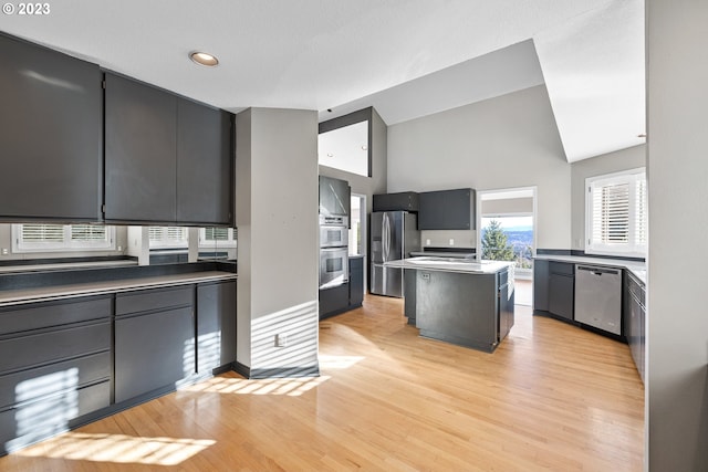 kitchen featuring a warming drawer, high vaulted ceiling, a center island, stainless steel appliances, and light wood-style floors