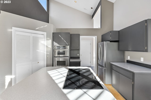 kitchen with a high ceiling, gray cabinets, appliances with stainless steel finishes, and light wood-type flooring