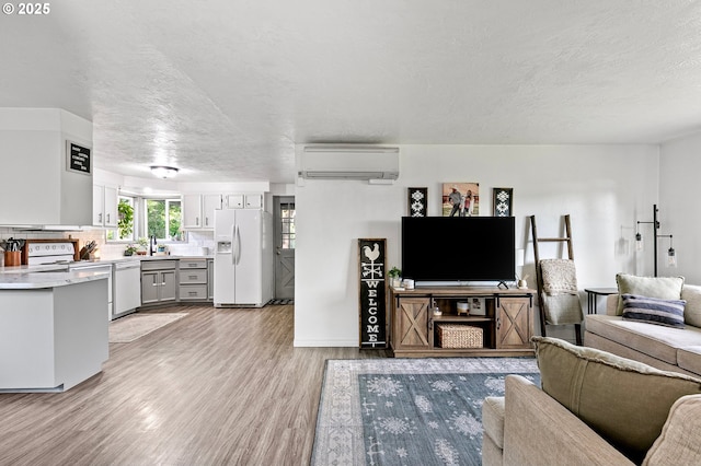 living room featuring a wall unit AC, light wood-style flooring, a textured ceiling, and baseboards