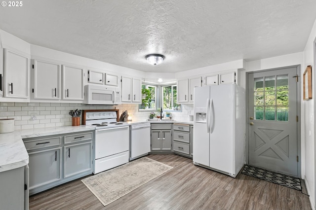 kitchen with white appliances, gray cabinetry, wood finished floors, decorative backsplash, and a sink