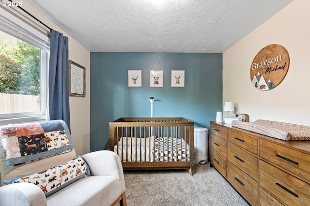 bedroom with light carpet, a nursery area, and a textured ceiling
