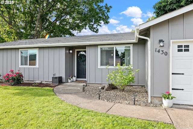 entrance to property featuring board and batten siding, a yard, central AC, and a garage