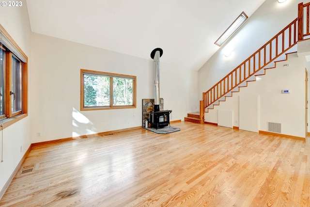 unfurnished living room featuring a skylight, a wood stove, and light wood-type flooring