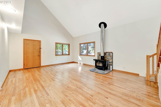 unfurnished living room featuring high vaulted ceiling, a wood stove, and light hardwood / wood-style flooring