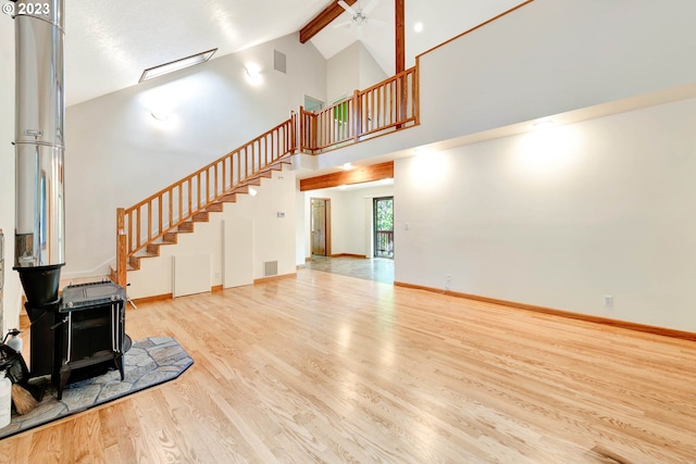 living room with high vaulted ceiling, light hardwood / wood-style floors, ceiling fan, and a wood stove