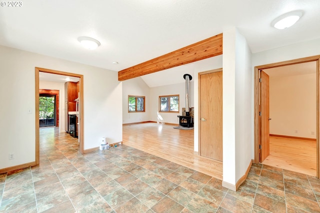 tiled empty room with a healthy amount of sunlight, a wood stove, and lofted ceiling with beams