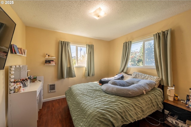 bedroom with heating unit, dark hardwood / wood-style flooring, and a textured ceiling