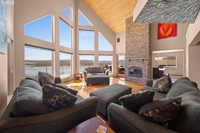 living room with high vaulted ceiling, light hardwood / wood-style floors, a water view, wooden ceiling, and a stone fireplace