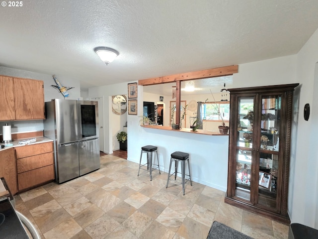 2951 NE Yount Ave, Roseburg, OR 97470 - kitchen featuring freestanding refrigerator, a textured ceiling, baseboards, brown cabinets, and stone finish flooring