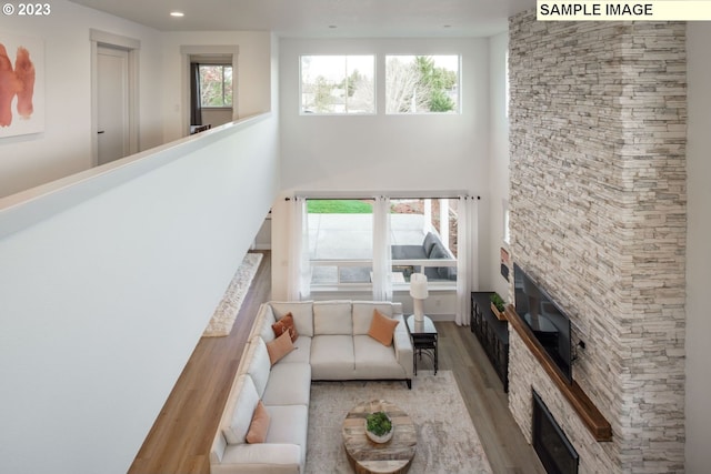 living room featuring a high ceiling, a stone fireplace, plenty of natural light, and light hardwood / wood-style flooring