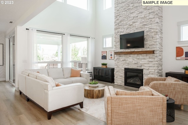 living room with a stone fireplace, a towering ceiling, and light hardwood / wood-style flooring