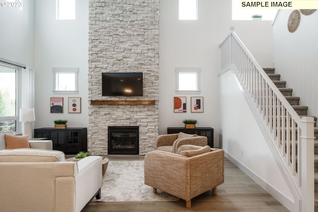 living room featuring a healthy amount of sunlight, a fireplace, a high ceiling, and light wood-type flooring