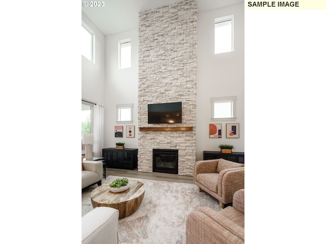 living room with a stone fireplace, a towering ceiling, and light wood-type flooring