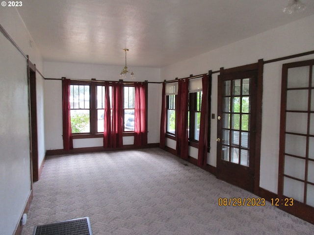 carpeted empty room featuring plenty of natural light, a notable chandelier, and french doors