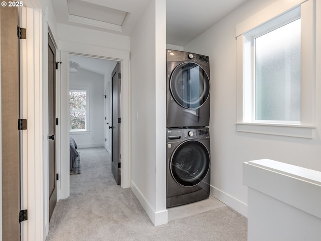 clothes washing area featuring baseboards, light colored carpet, attic access, laundry area, and stacked washer and clothes dryer