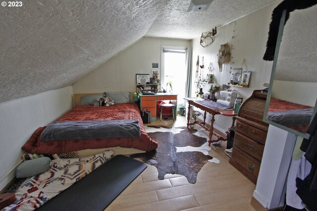 bedroom with lofted ceiling, a textured ceiling, and light wood-type flooring