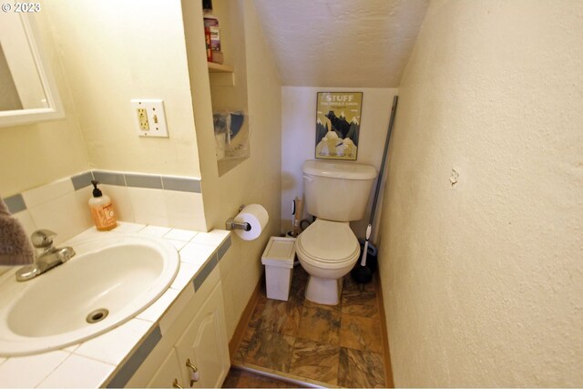 bathroom featuring vanity, vaulted ceiling, a textured ceiling, and toilet