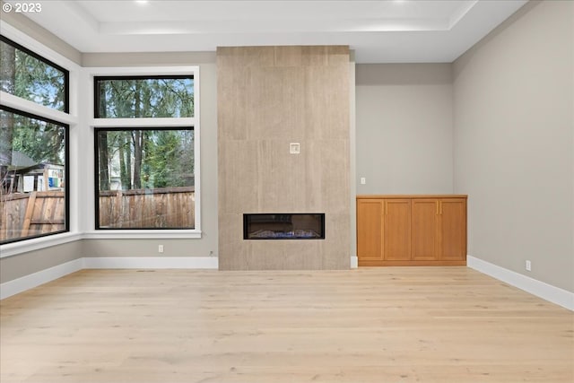 unfurnished living room featuring a large fireplace, light hardwood / wood-style floors, and a tray ceiling