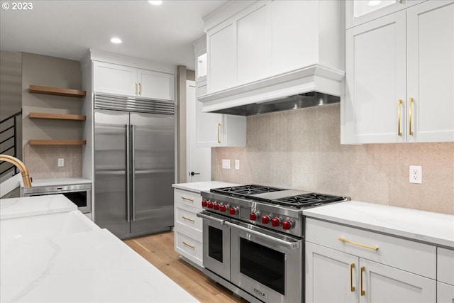 kitchen featuring white cabinets, premium appliances, light stone countertops, and light hardwood / wood-style flooring