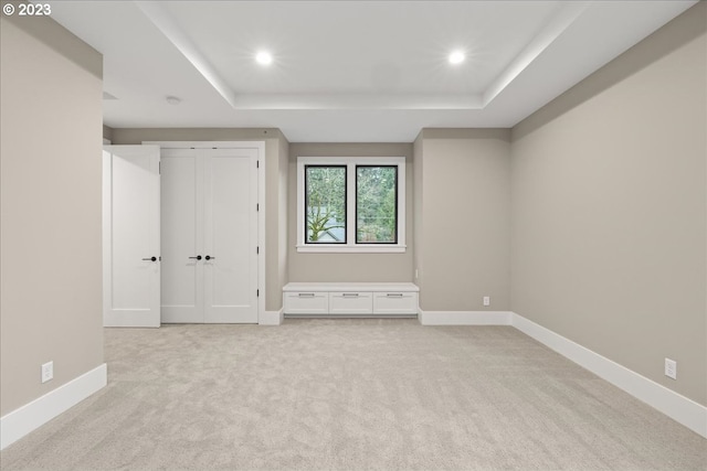 unfurnished bedroom with light carpet and a tray ceiling