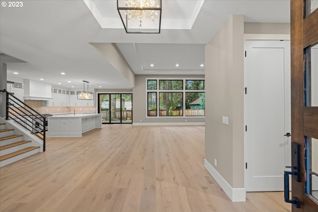 entrance foyer featuring a tray ceiling, a chandelier, and light hardwood / wood-style floors