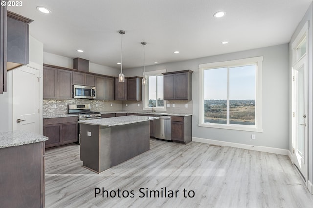 kitchen with light stone countertops, decorative light fixtures, light wood-type flooring, stainless steel appliances, and a center island