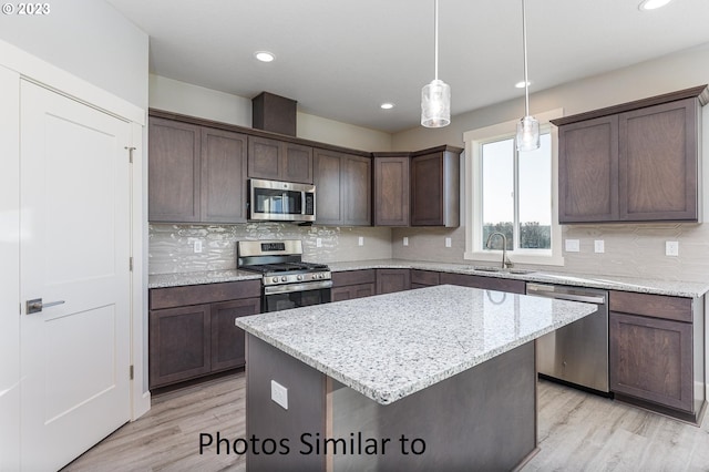 kitchen with stainless steel appliances, a center island, light wood-type flooring, and sink