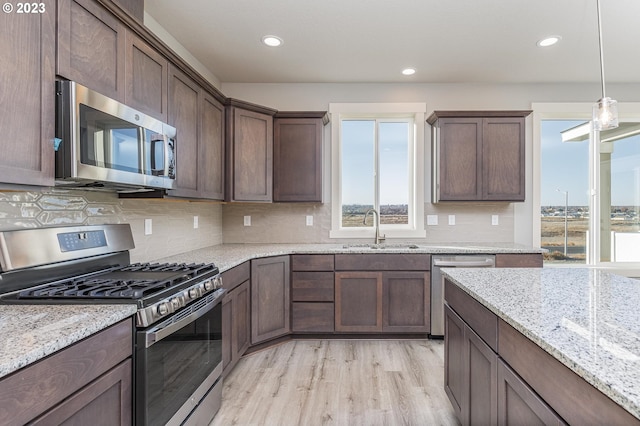 kitchen featuring stainless steel appliances, light stone countertops, backsplash, light wood-type flooring, and sink