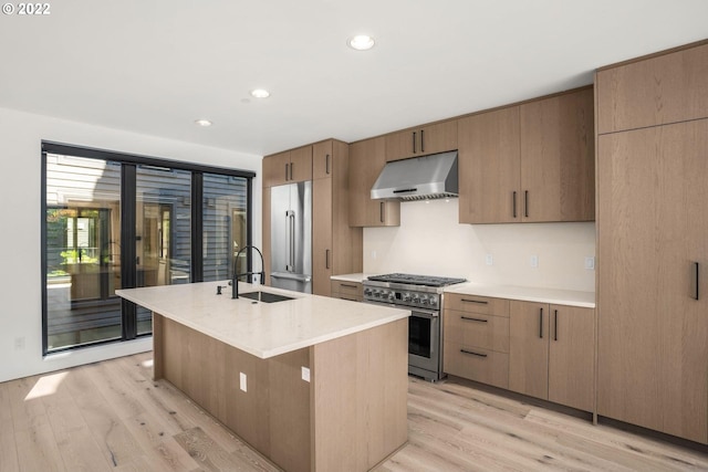 kitchen with premium appliances, a center island with sink, sink, and light hardwood / wood-style flooring