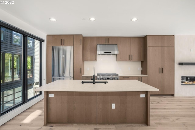 kitchen with plenty of natural light, an island with sink, light hardwood / wood-style floors, and stainless steel fridge