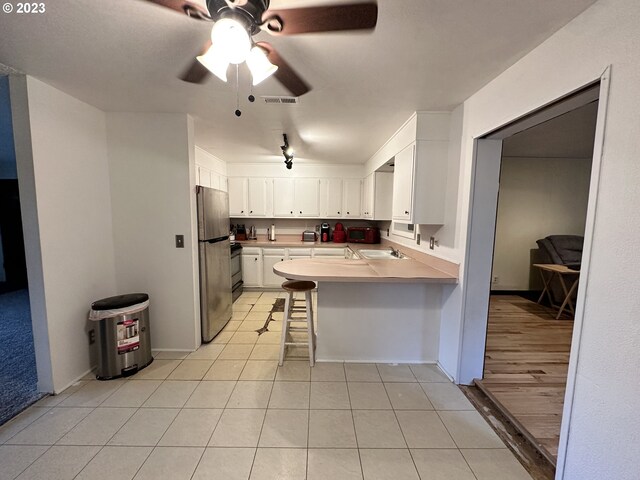 kitchen featuring appliances with stainless steel finishes, white cabinetry, a kitchen bar, light tile patterned floors, and kitchen peninsula