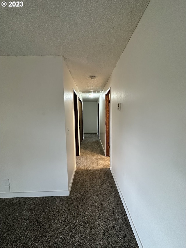 hallway featuring dark colored carpet and a textured ceiling