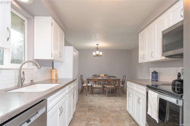 kitchen featuring hanging light fixtures, stainless steel appliances, a notable chandelier, white cabinetry, and sink