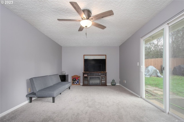 living area with ceiling fan, carpet, a textured ceiling, and a fireplace